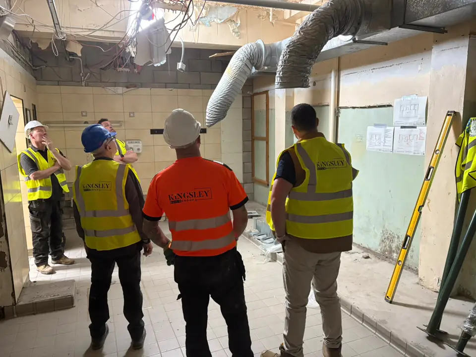 Five Kingsley operatives in a stripped-out room, drawings on the wall, ahead of a refit